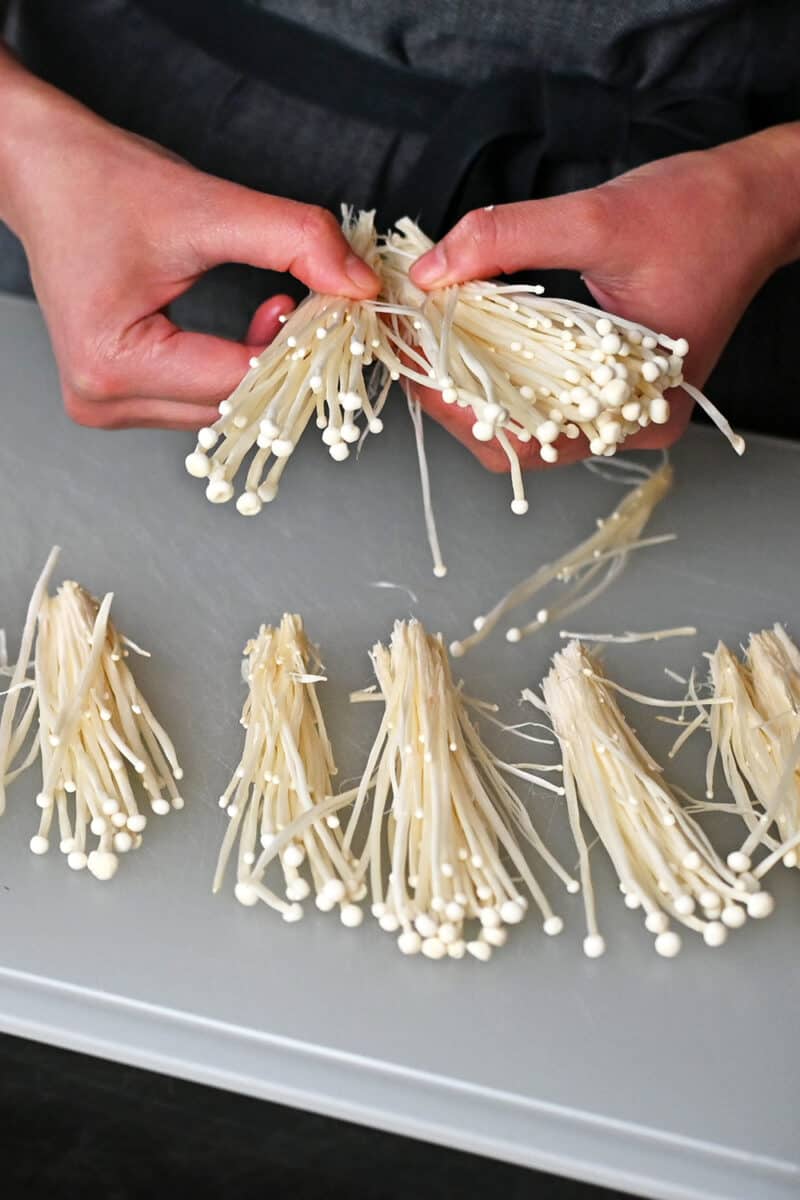 A person is using their hands to carefully separate enoki mushrooms into small bundles.