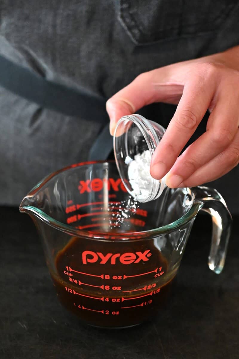 Adding arrowroot powder into a measuring cup filled with All-Purpose Stir-Fry Sauce