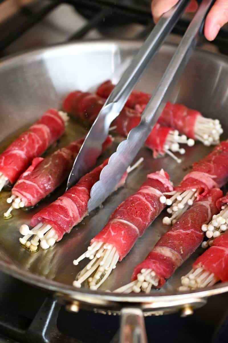 Frying beef and enoki mushroom rolls in a frying pan.