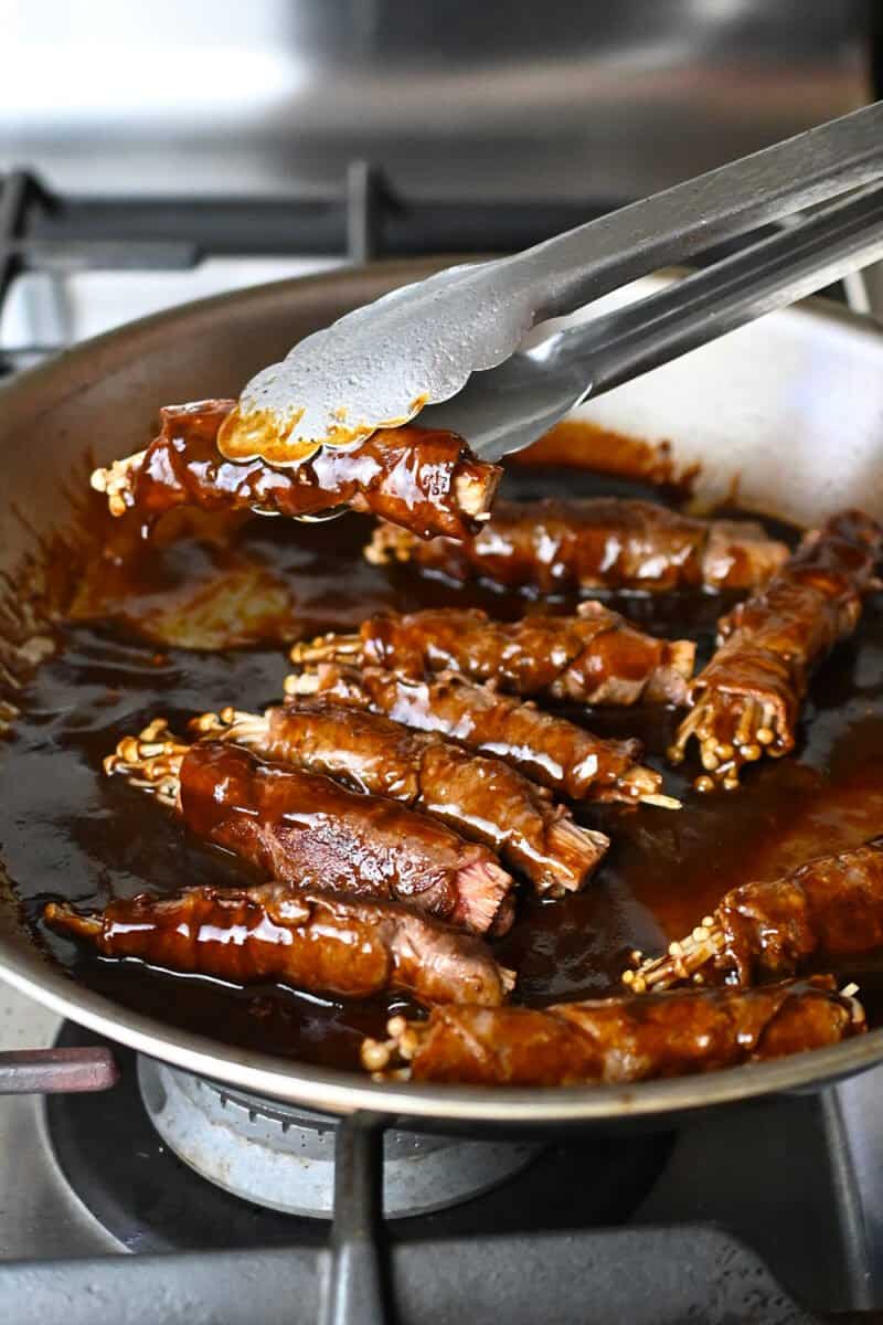 Adding beef and enoki rolls to a skillet filled with a thickened brown sauce.