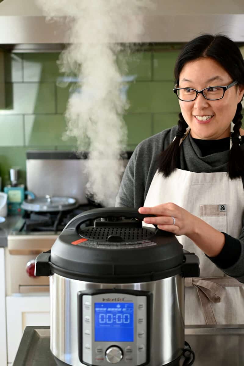 A smiling Asian woman is depressurizing her Instant Pot.