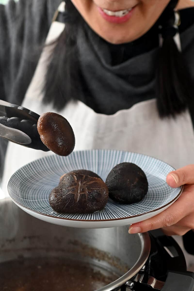 A smiling Asian is placing cooked shiitake mushrooms on a blue and white plate