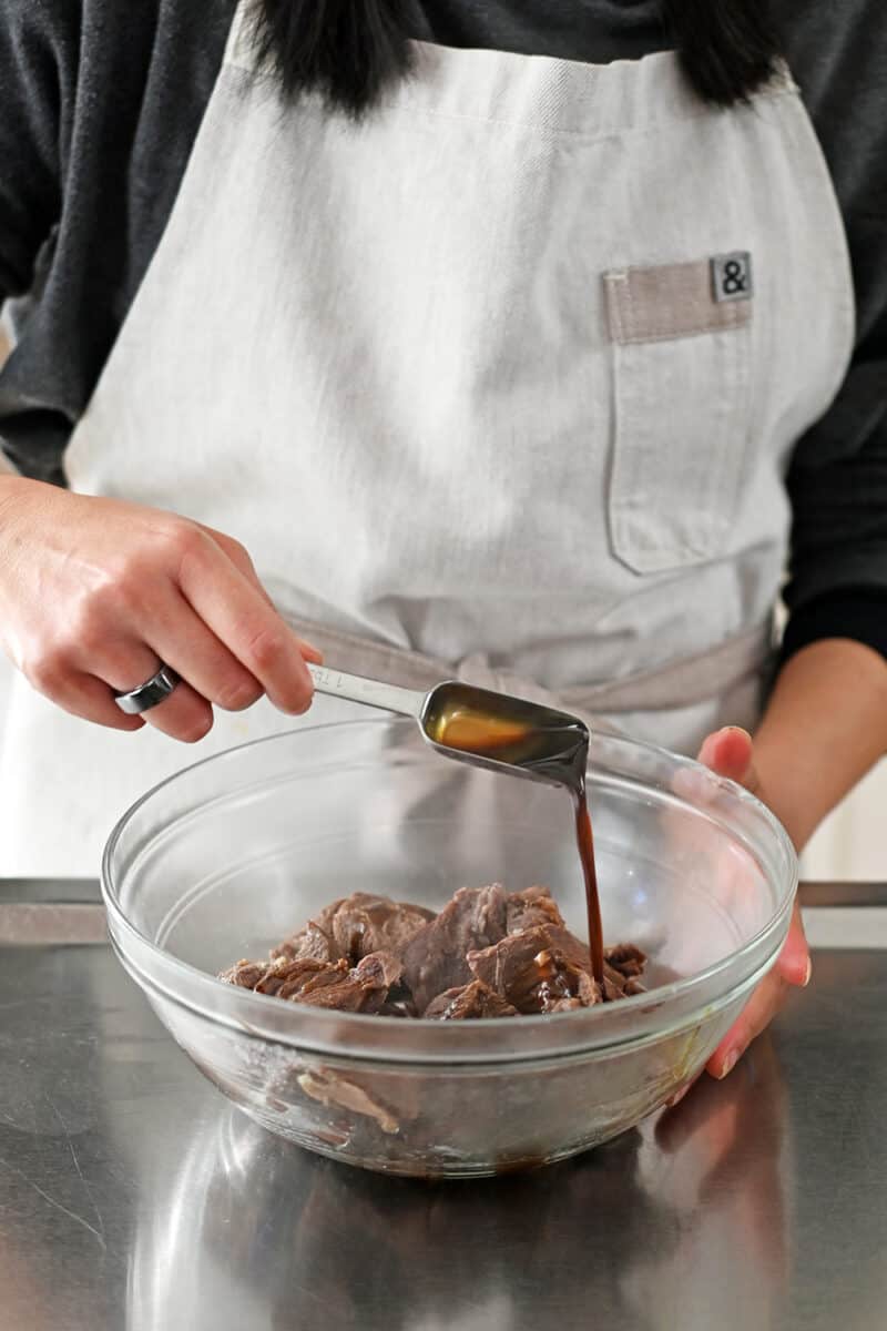 Adding a spoonful of coconut aminos in a bowl of stewed beef cubes.