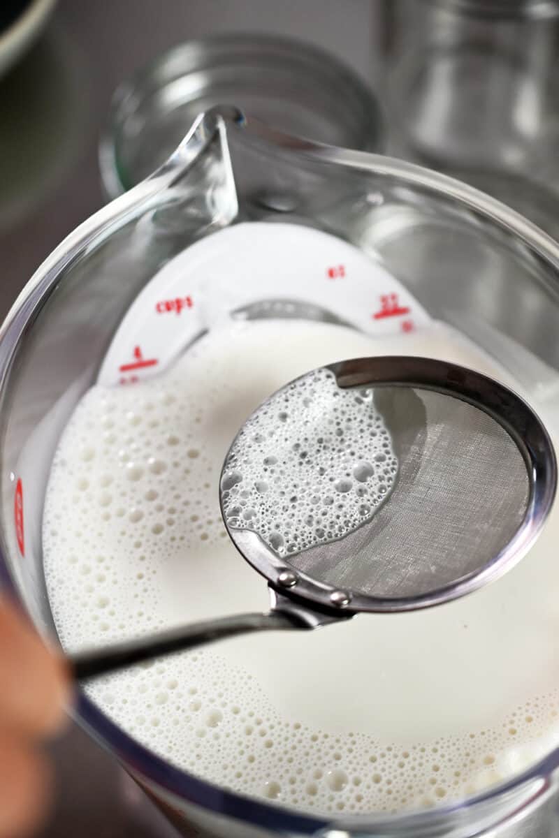 Using a small mesh sieve to remove the bubbles from the top of the hot coconut milk mixture