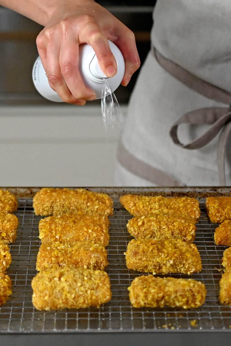 Spraying a wire rack covered with fish sticks with avocado oil spray