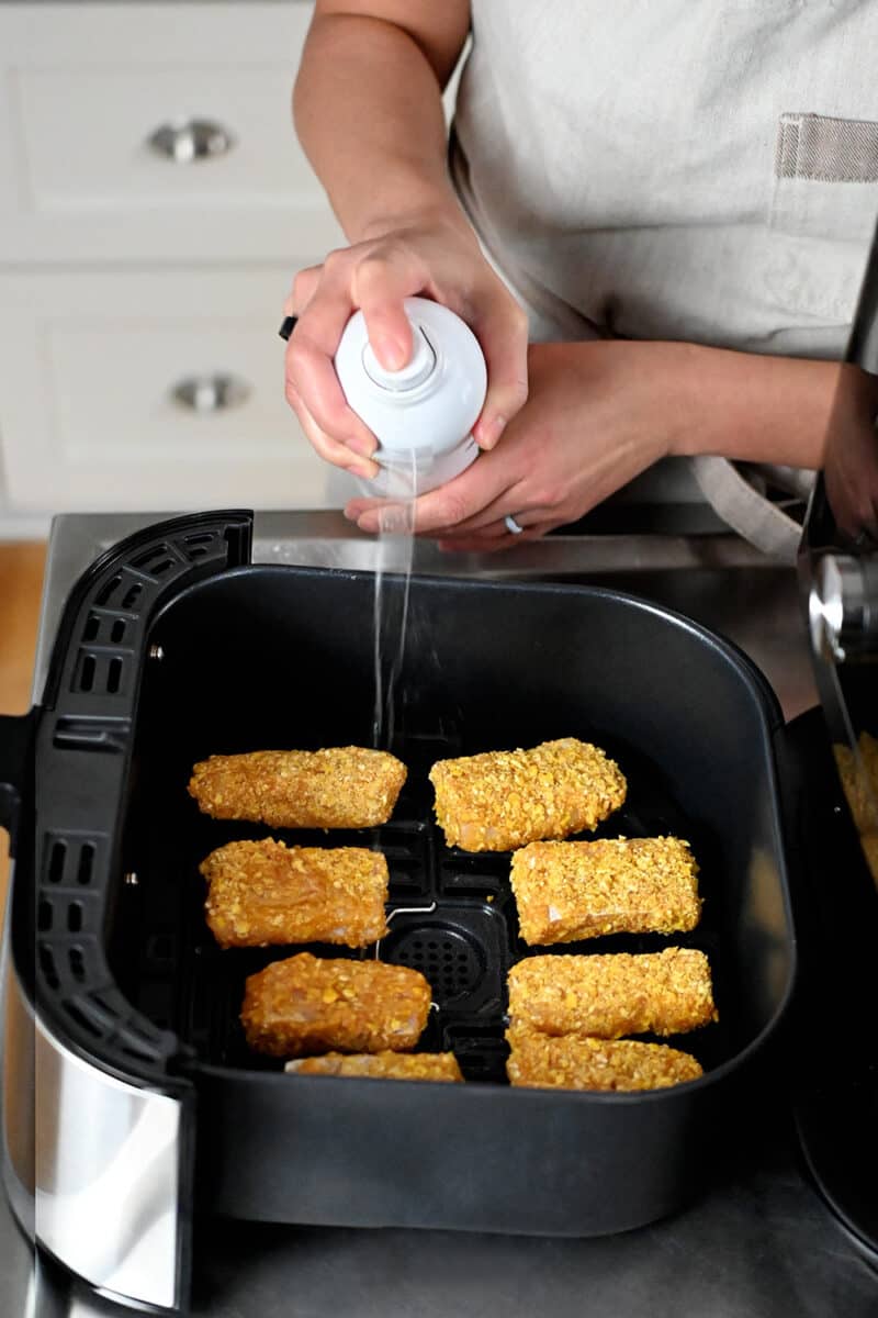 Spraying avocado oil on fish sticks in an air fryer basket