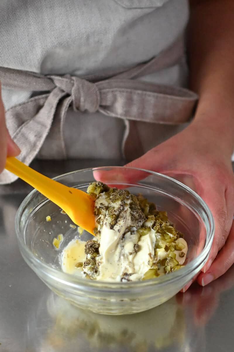 Someone mixing tartar sauce in a clear bowl.