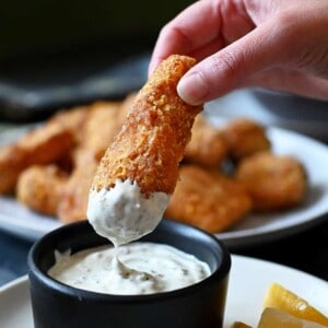 A hand is dipping a fish stick in tartar sauce