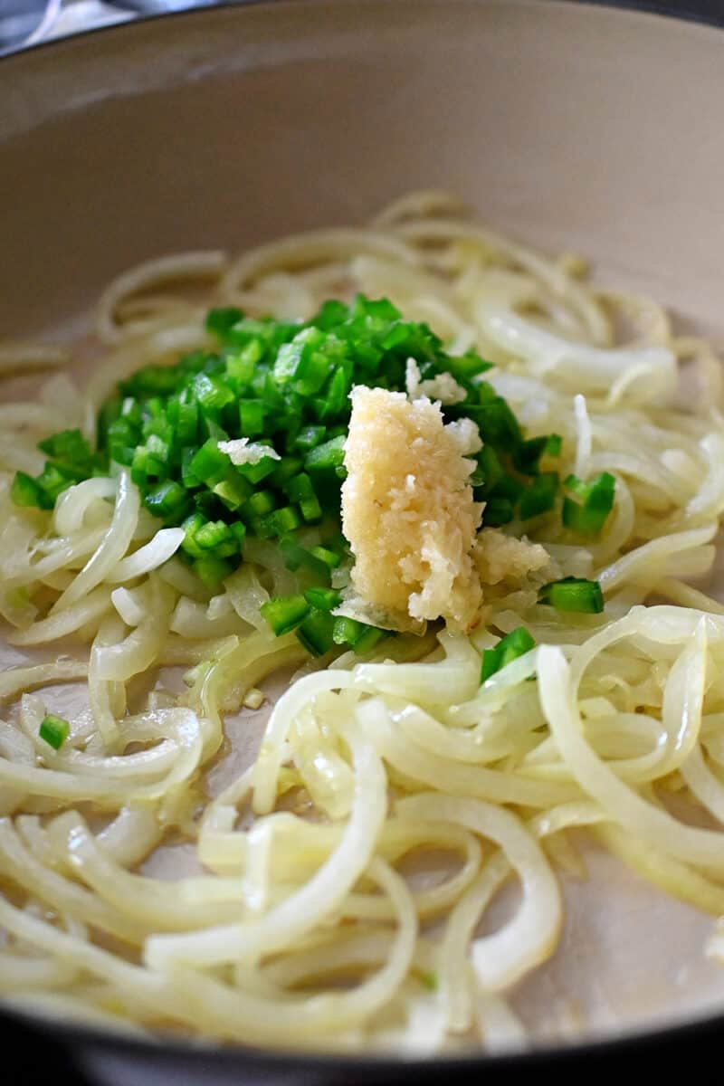 A closeup of softened onions, minced jalapeño peppers, and minced garlic.