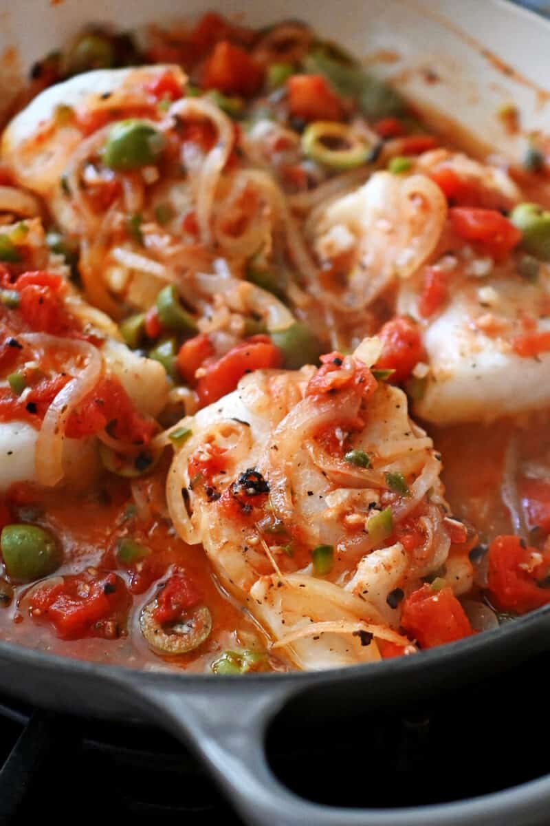 A closeup of cooked fish filets in homemade Veracruz sauce