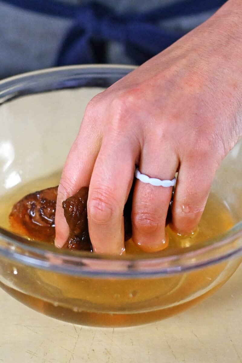 A hand is grabbing some dried shiitake mushrooms from a bowl of water.