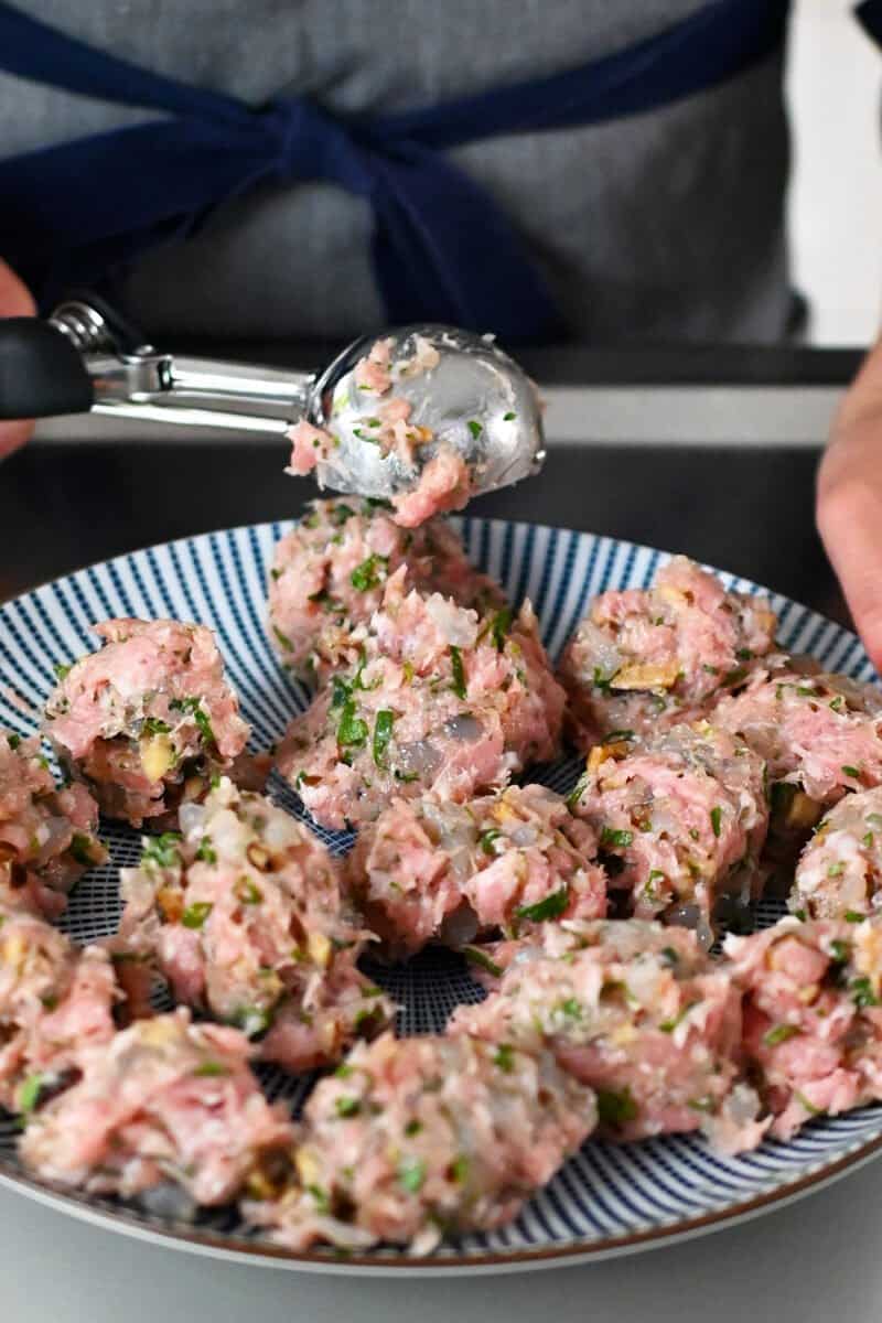 A medium ice cream scoop is used to portion out wonton meatballs on a blue and white plate.
