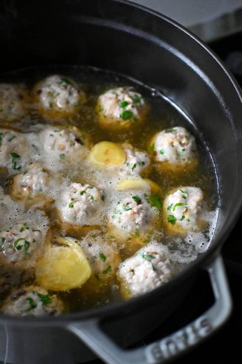 Wonton Meatballs simmering in a gingery chicken broth in a large pot.
