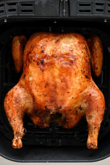 An overhead shot of a golden brown air fryer whole chicken in an air fryer basket.