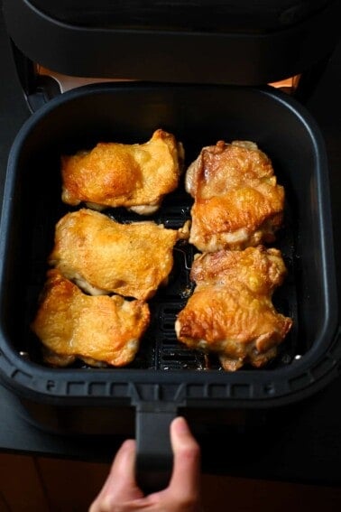 An overhead shot of crispy air fryer chicken thighs in an open air fryer basket.