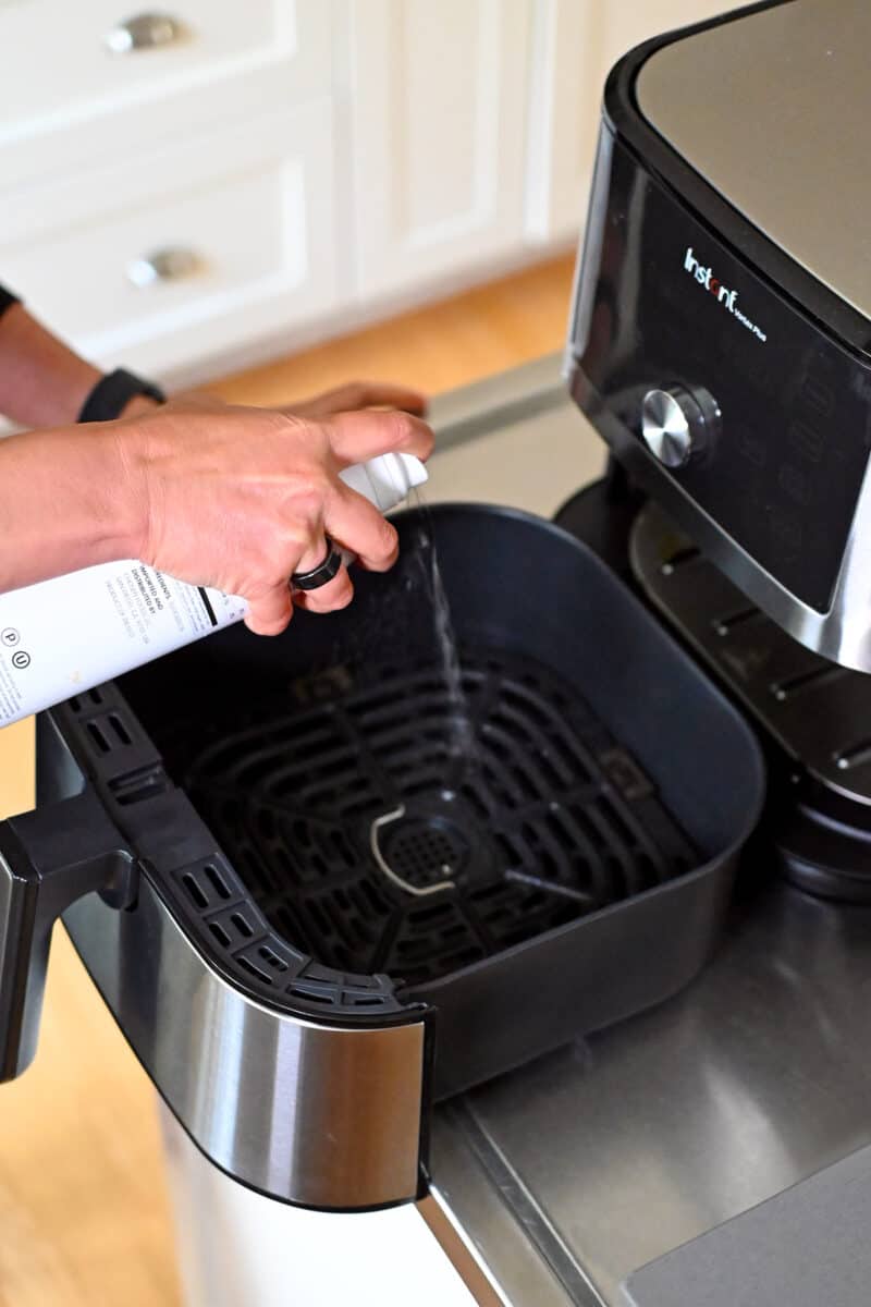 Spraying avocado oil into an open air fryer basket. 