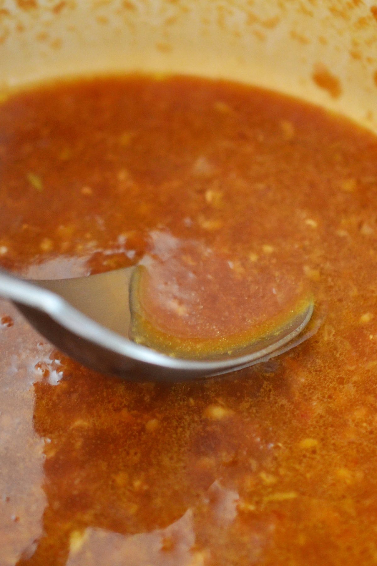 A spoon is scooping up some Asian citrus dressing in a saucepan.