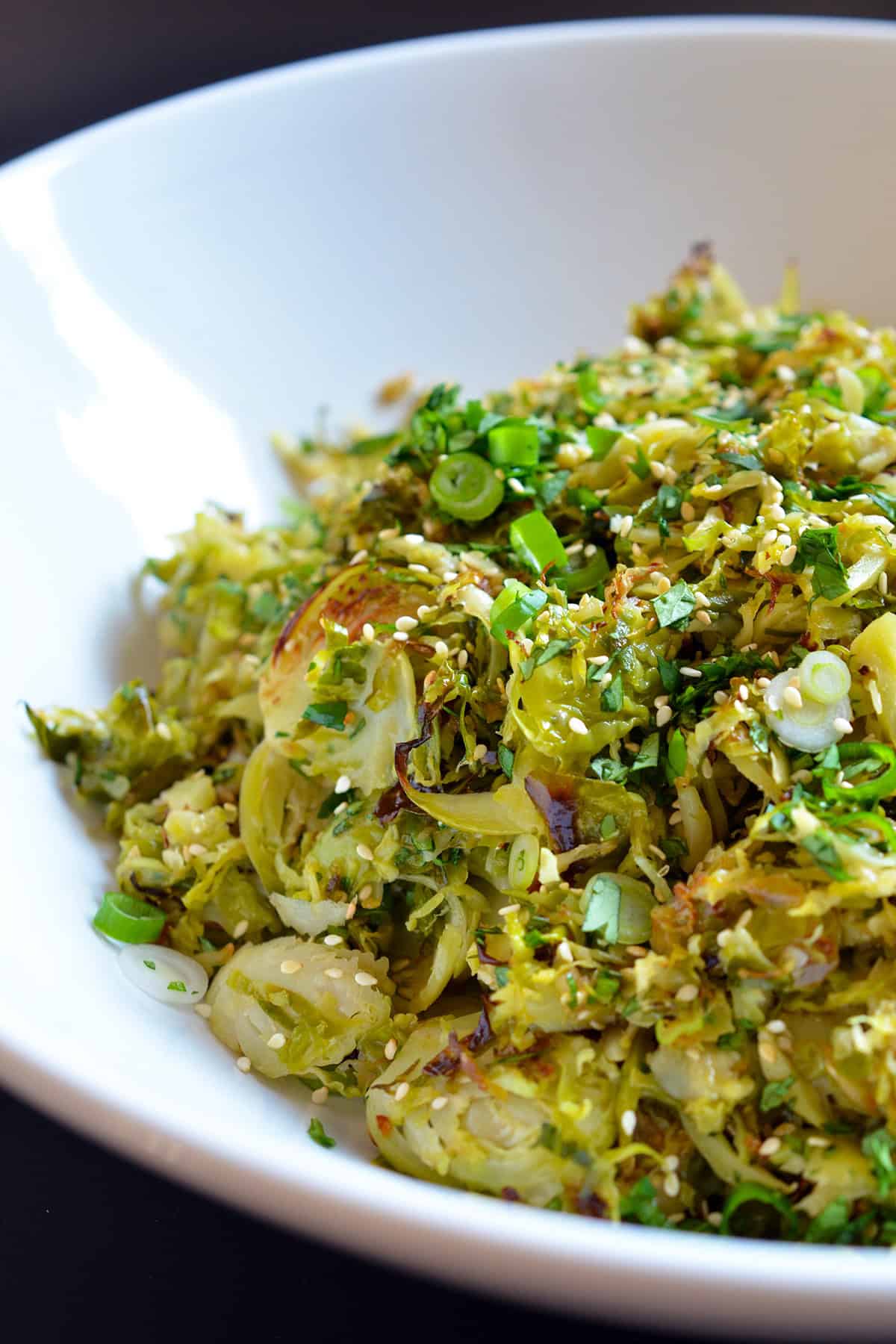 A closeup of a large white serving bowl filled with Roasted Brussels Sprouts Salad with Asian Citrus Dressing.