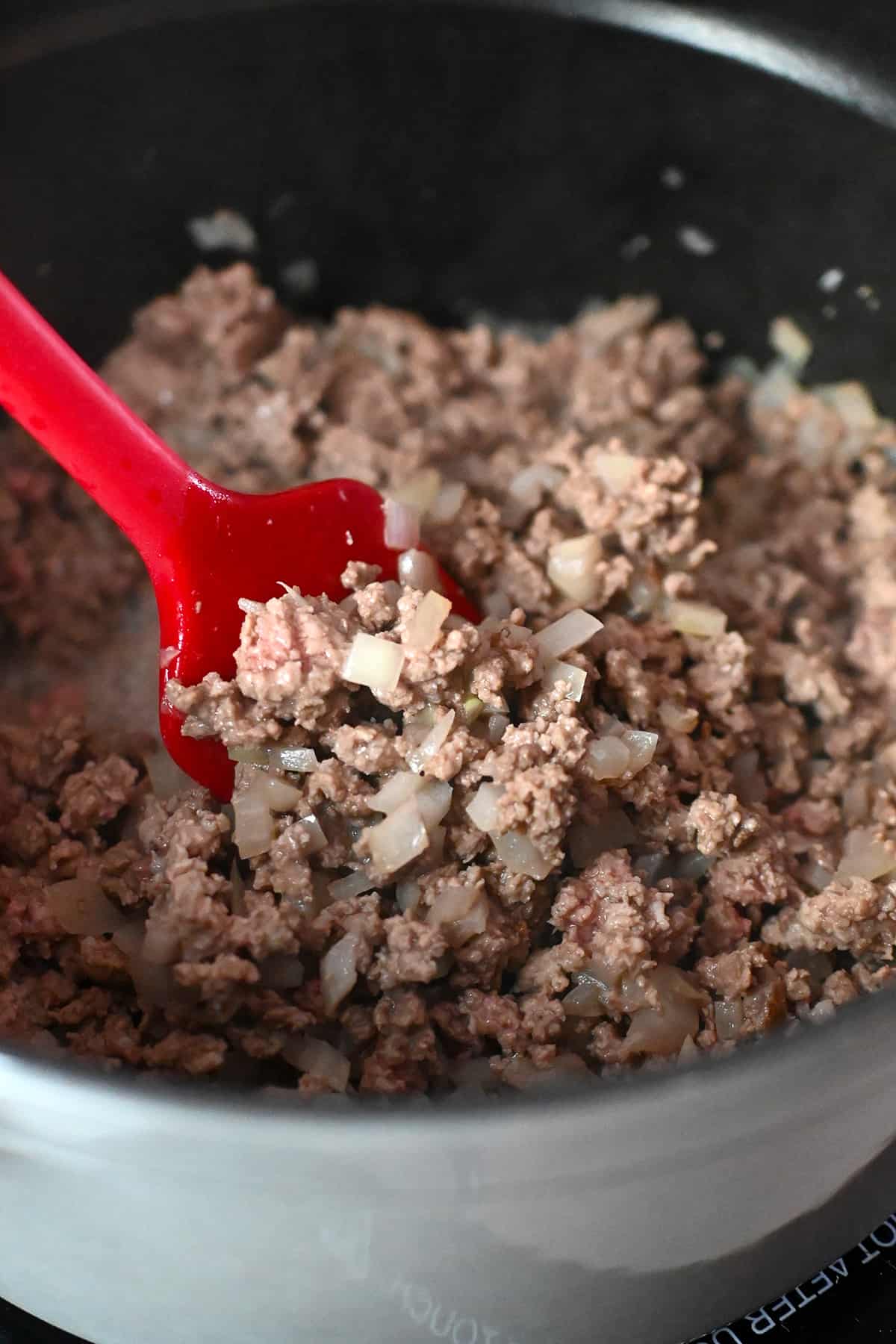 A close up shot of cooked ground beef and ground pork and diced onions in a gray stock pot.