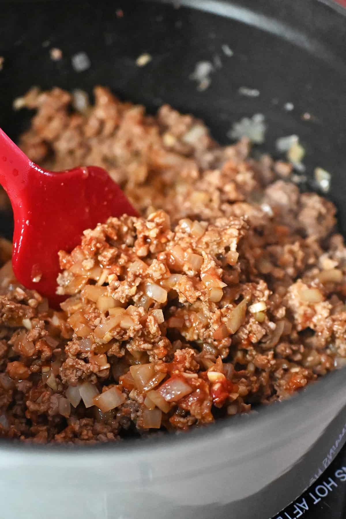 A closeup of seasoned ground meat and onions in a gray stock pot to make cabbage roll soup.