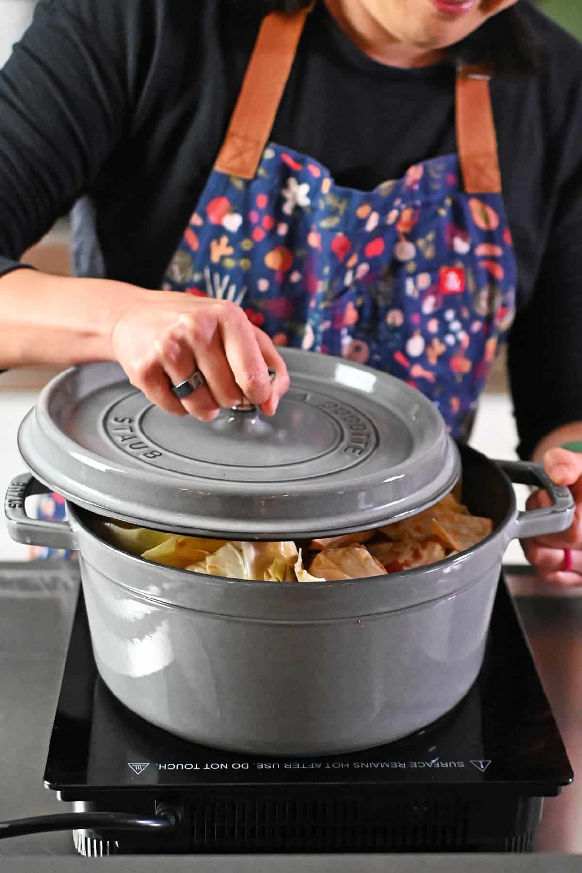 Placing a lid on top of a gray stockpot filled with cabbage roll soup.