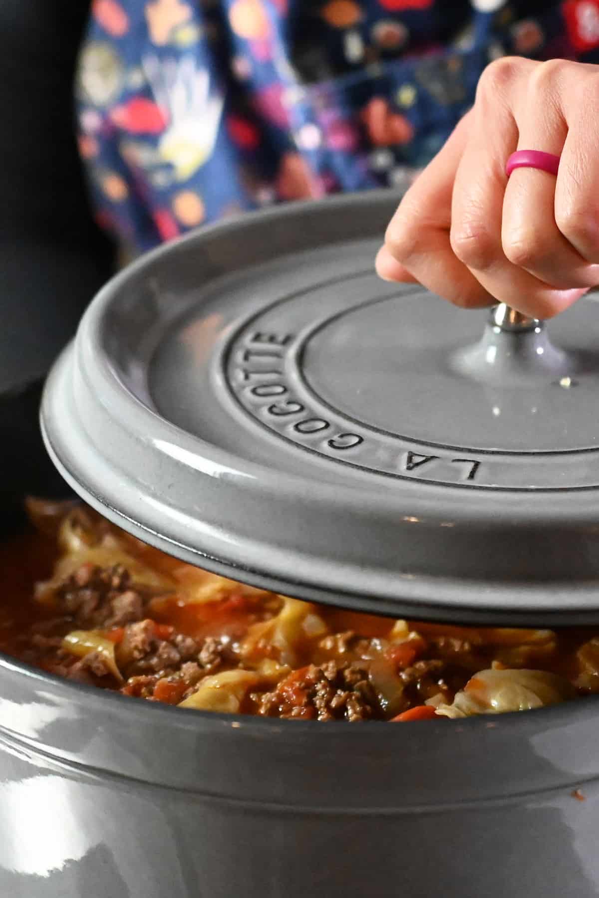 Removing the lid on a gray stockpot filled with cabbage roll soup.