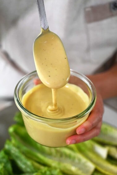 A spoon dipping into a jar of dairy-free Caesar Dressing.