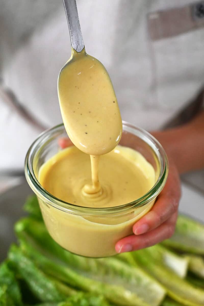 A spoon dipping into a jar of dairy-free Caesar Dressing.