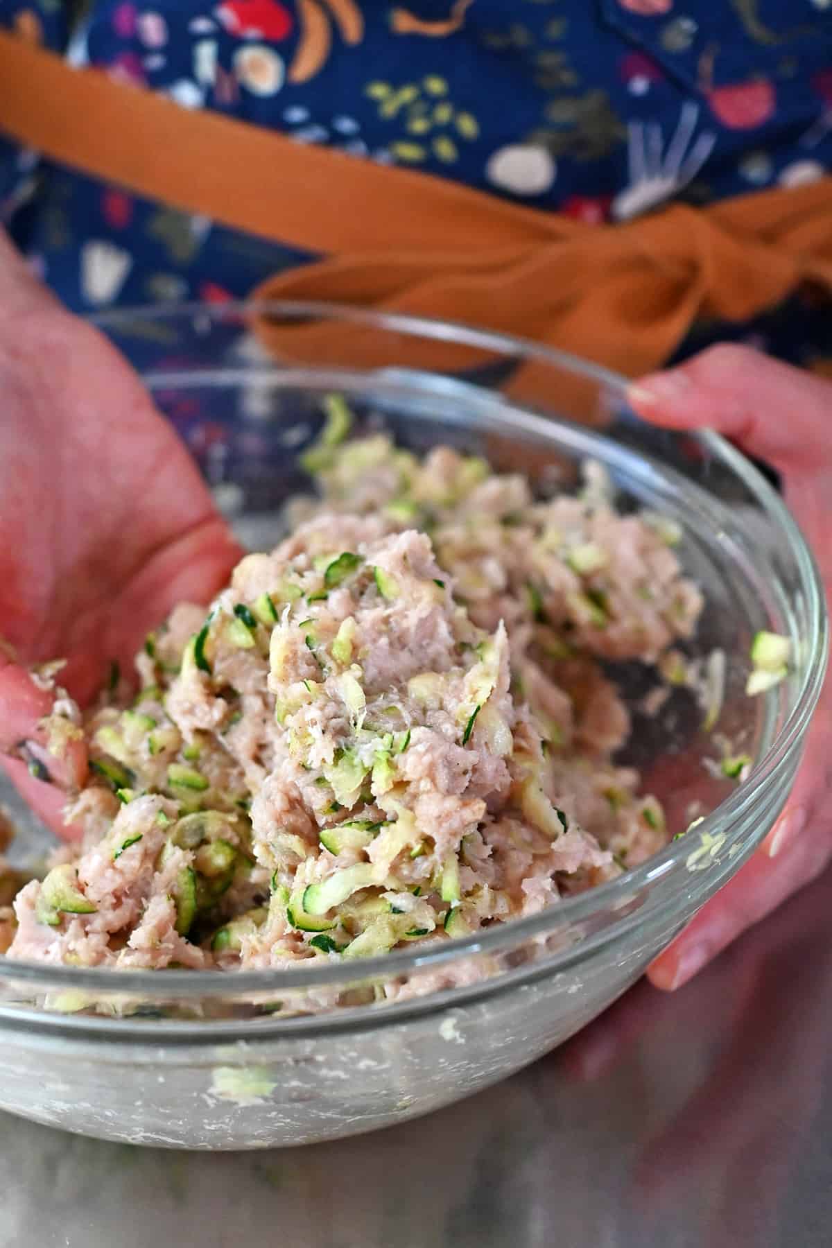 Mixing the chicken meatball mixture in a glass bowl with clean hands.