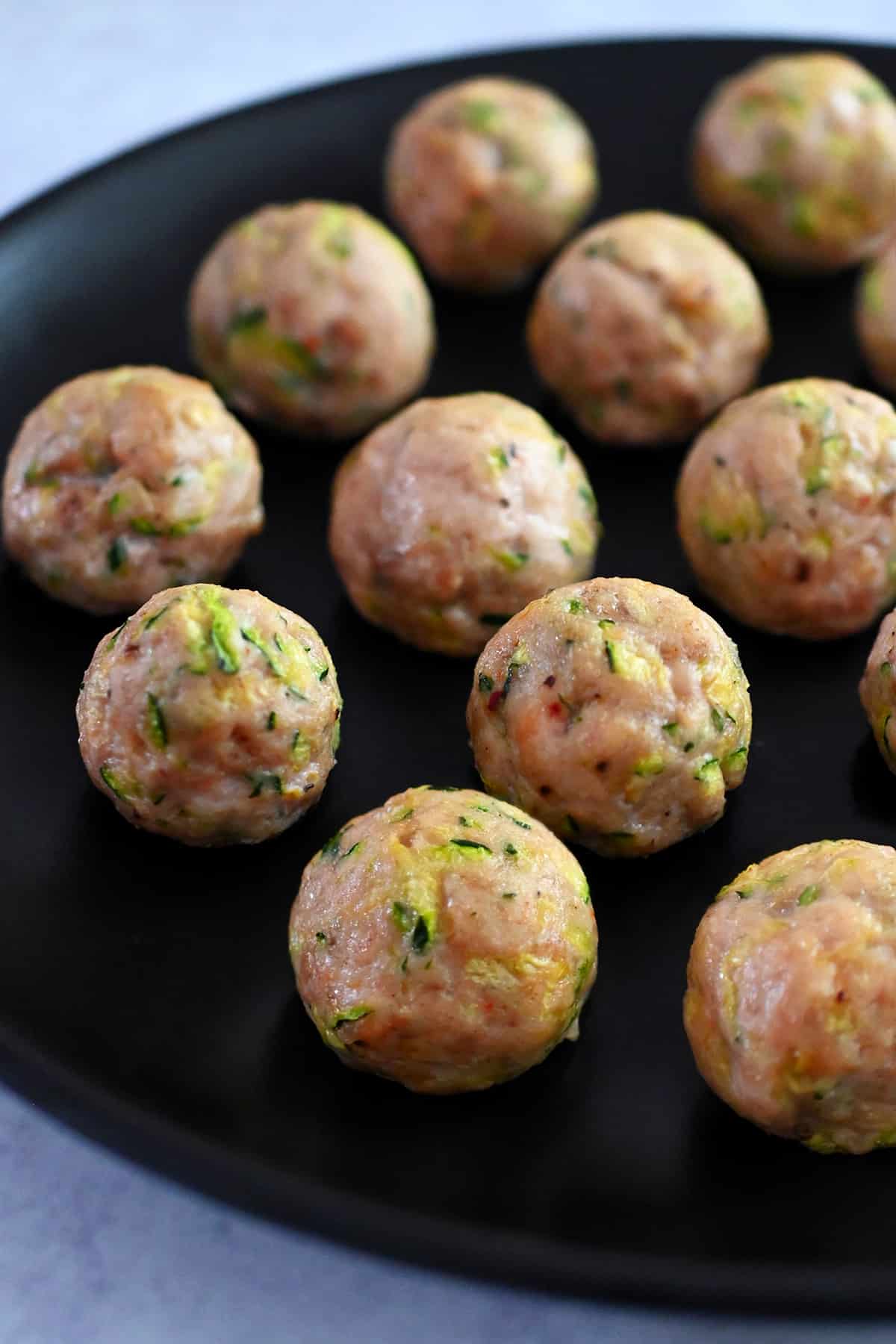 A black plate topped with paleo baked chicken meatballs made with shredded zucchini.
