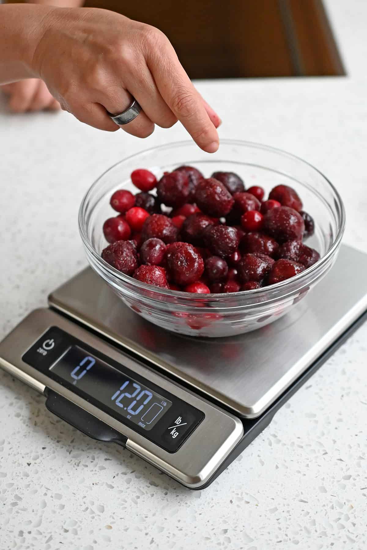 Measuring frozen cranberries and cherries in a glass bowl on a kitchen scale to make paleo cranberry sauce.