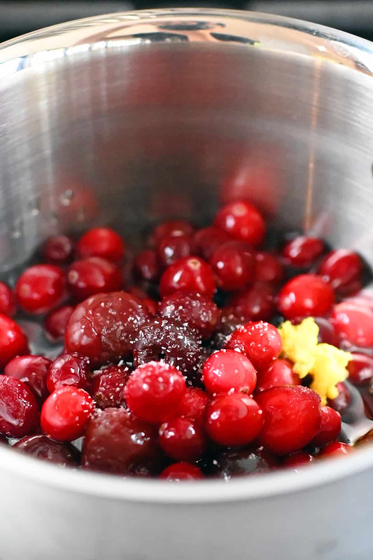 A closeup of a saucepan filled with frozen cherries, cranberries, apple juice, minced ginger, and salt.