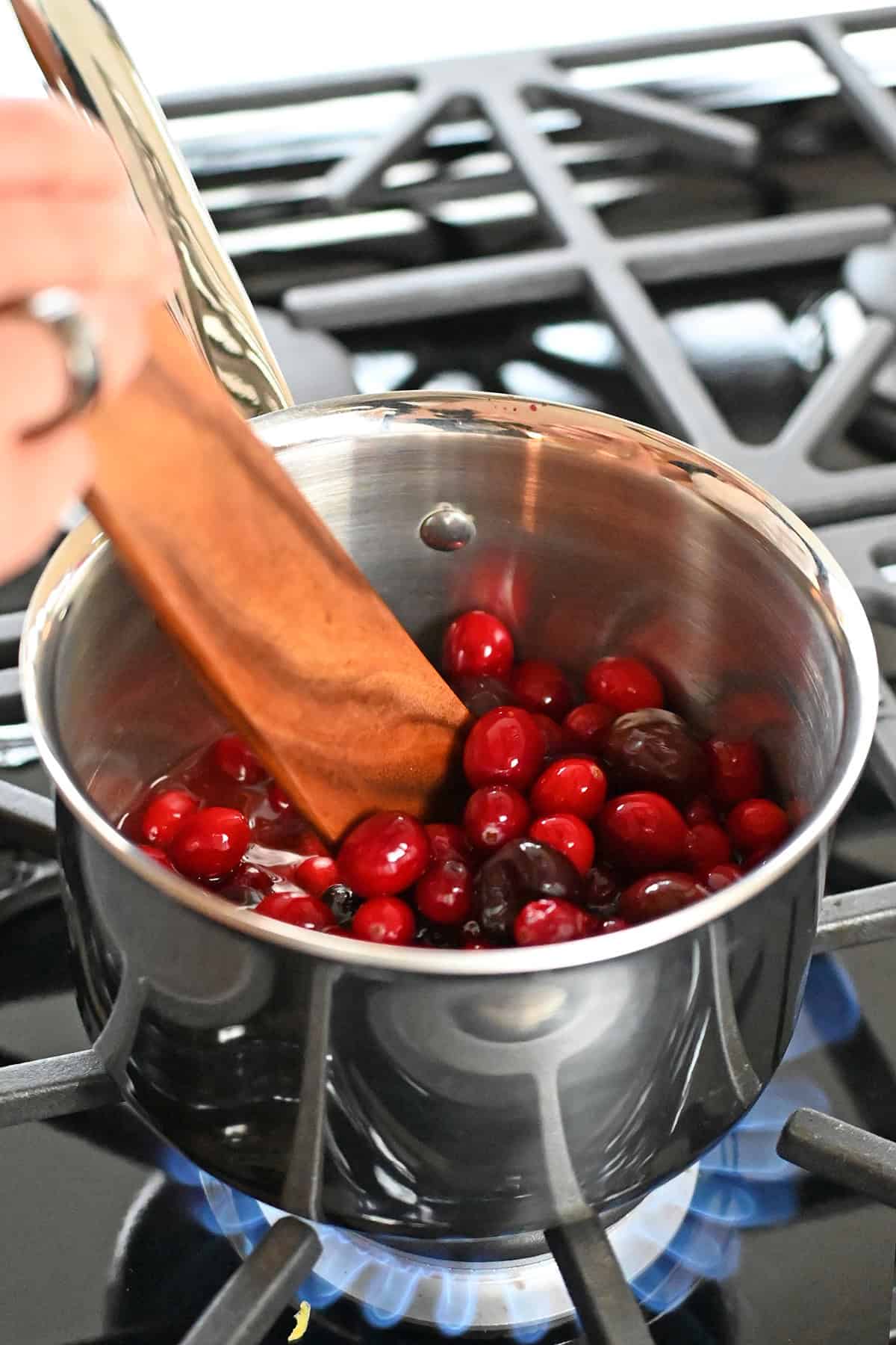 Stirring a saucepan filled with the ingredients for paleo cranberry cherry sauce on a gas burner.