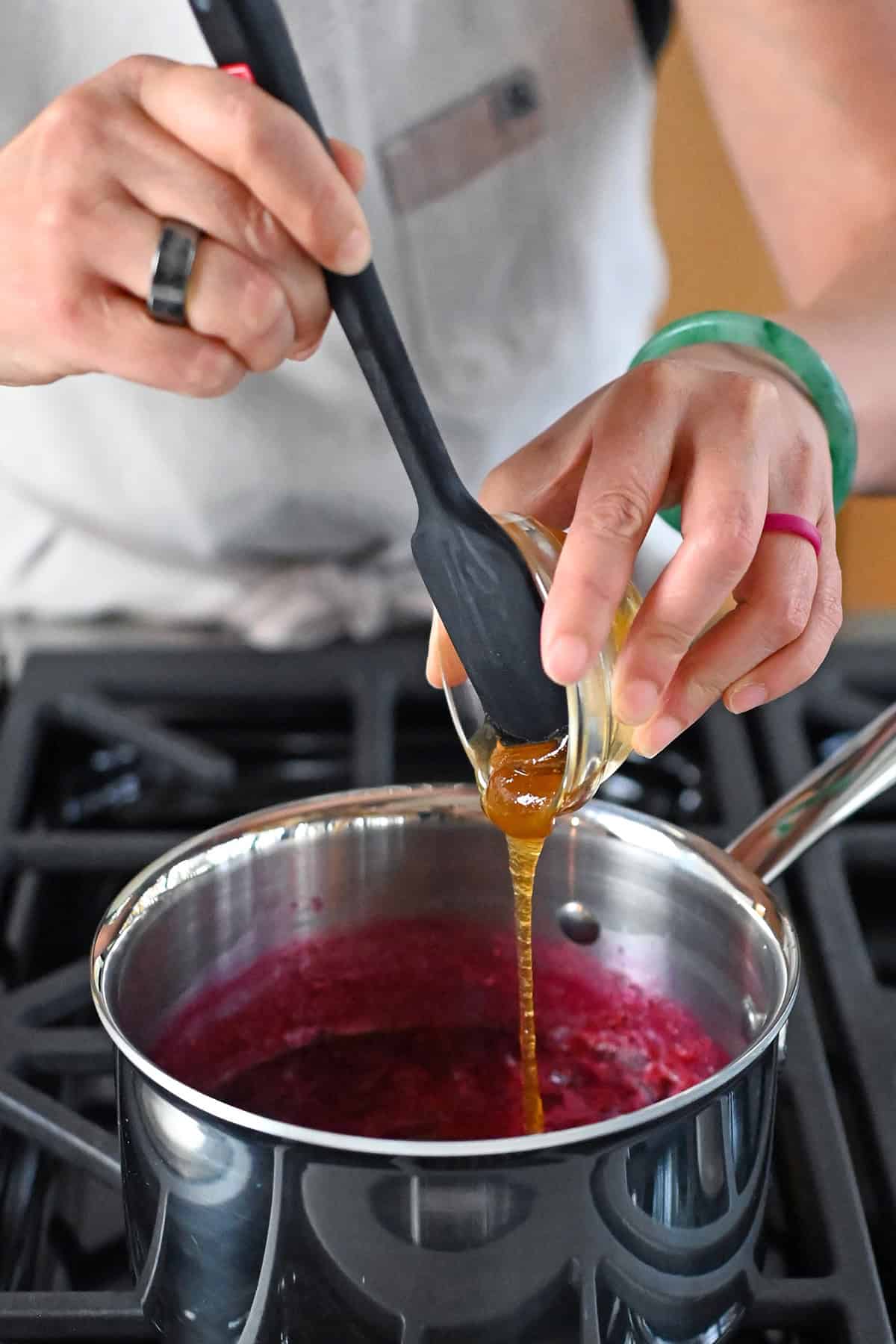 Adding honey to a saucepan filled with paleo cranberry cherry sauce.