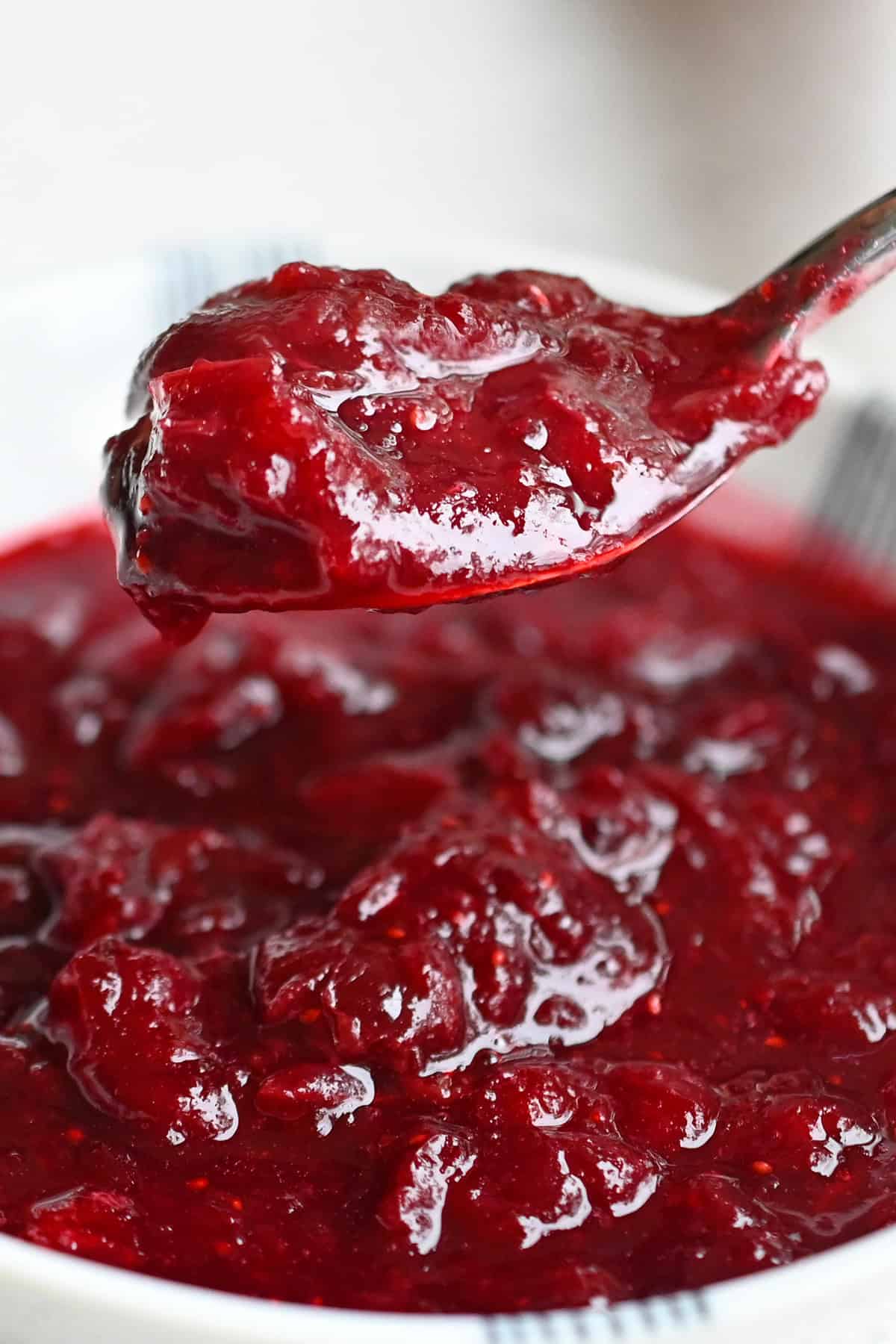 A bowl of homemade paleo cranberry sauce and a spoon lifting up a serving of it.