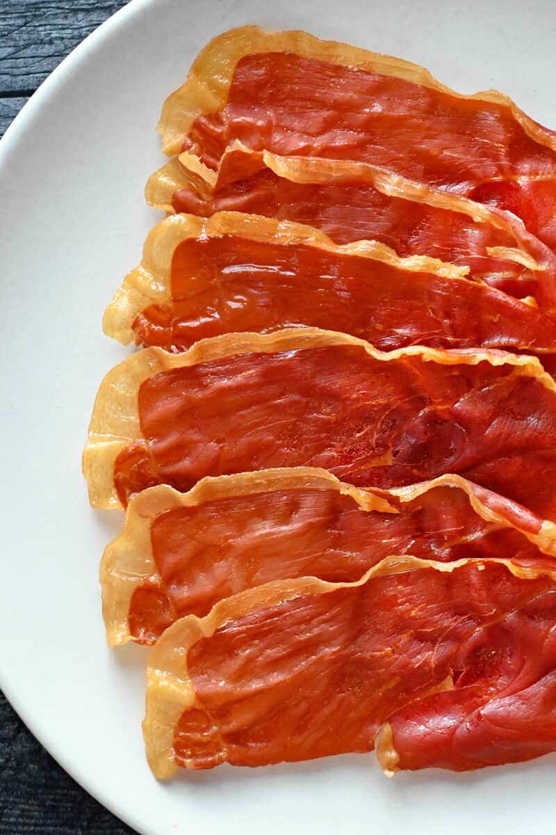A white plate topped with crispy prosciutto slices