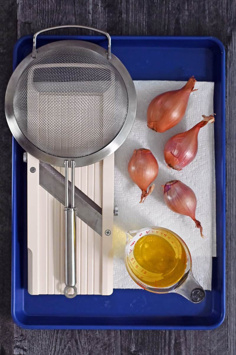 An overhead shot of the equipment and raw ingredients needed to make crispy shallots in the microwave.