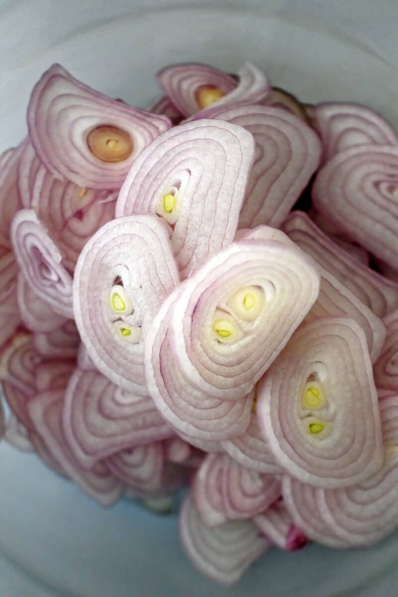 An overhead shot of a glass bowl filled with thinly diced shallots