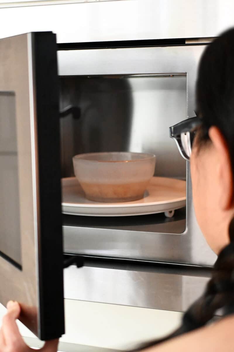 An open microwave filled with a bowl of sliced shallots and avocado oil