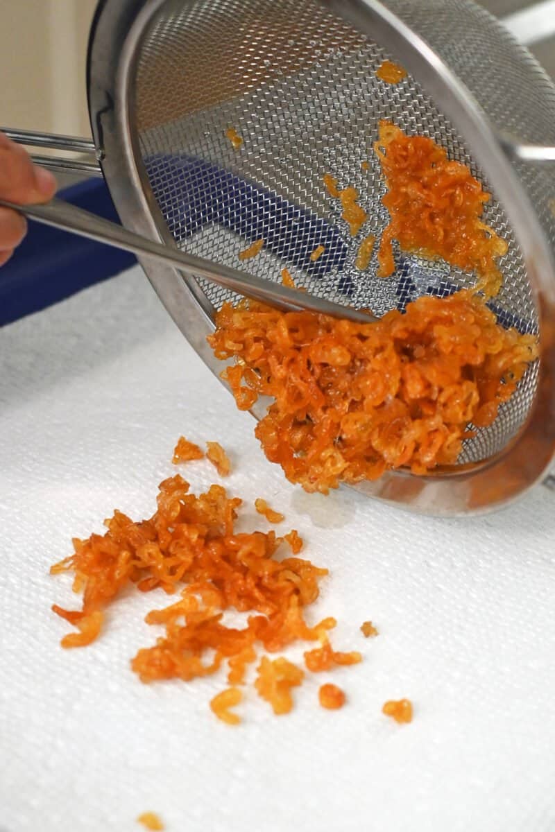 Transferring crispy shallots from a sieve to a paper towel lined rimmed baking sheet.