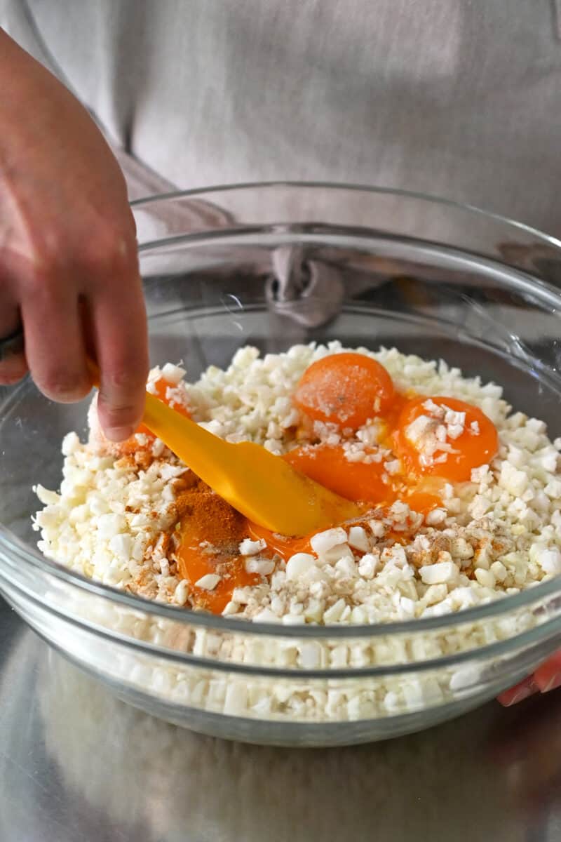 Combining cauliflower rice in a large bowl with egg yolks and seasoning to make golden cauliflower fried rice.
