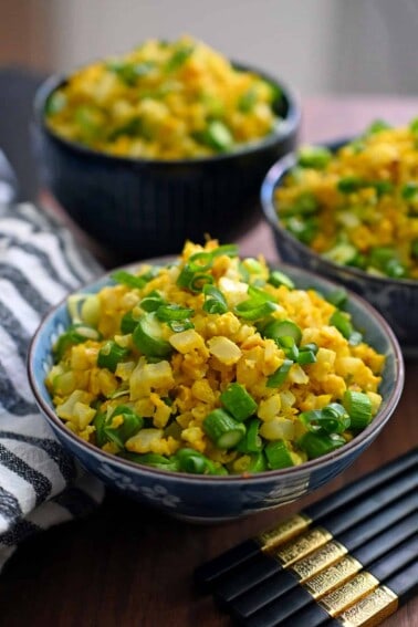 Three bowls of golden cauliflower fried rice, a paleo, whole30, and keto vegetable side dish.