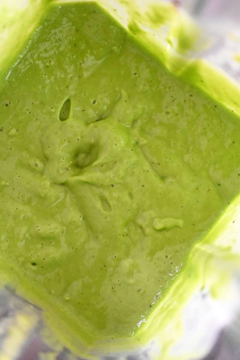 An overhead shot of an open Vitamix blender with a bright green Green Goddess Dressing inside.
