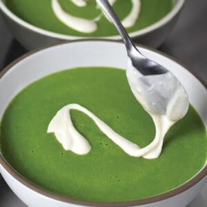 Adding a dairy-free cashew cream to the top of a bowl of pureed green soup.