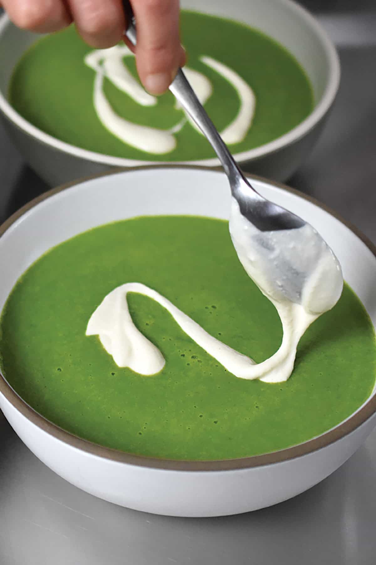 Adding a dairy-free cashew cream to the top of a bowl of pureed green soup.