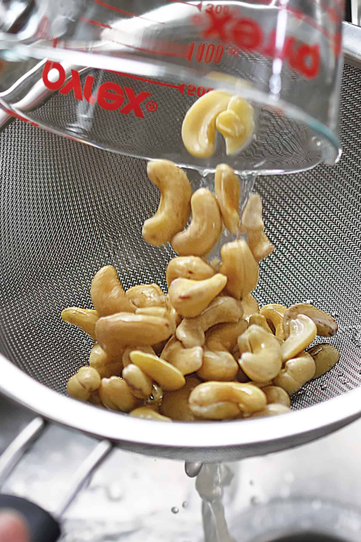 Pouring soaked raw cashews in a strainer to make cashew cream.