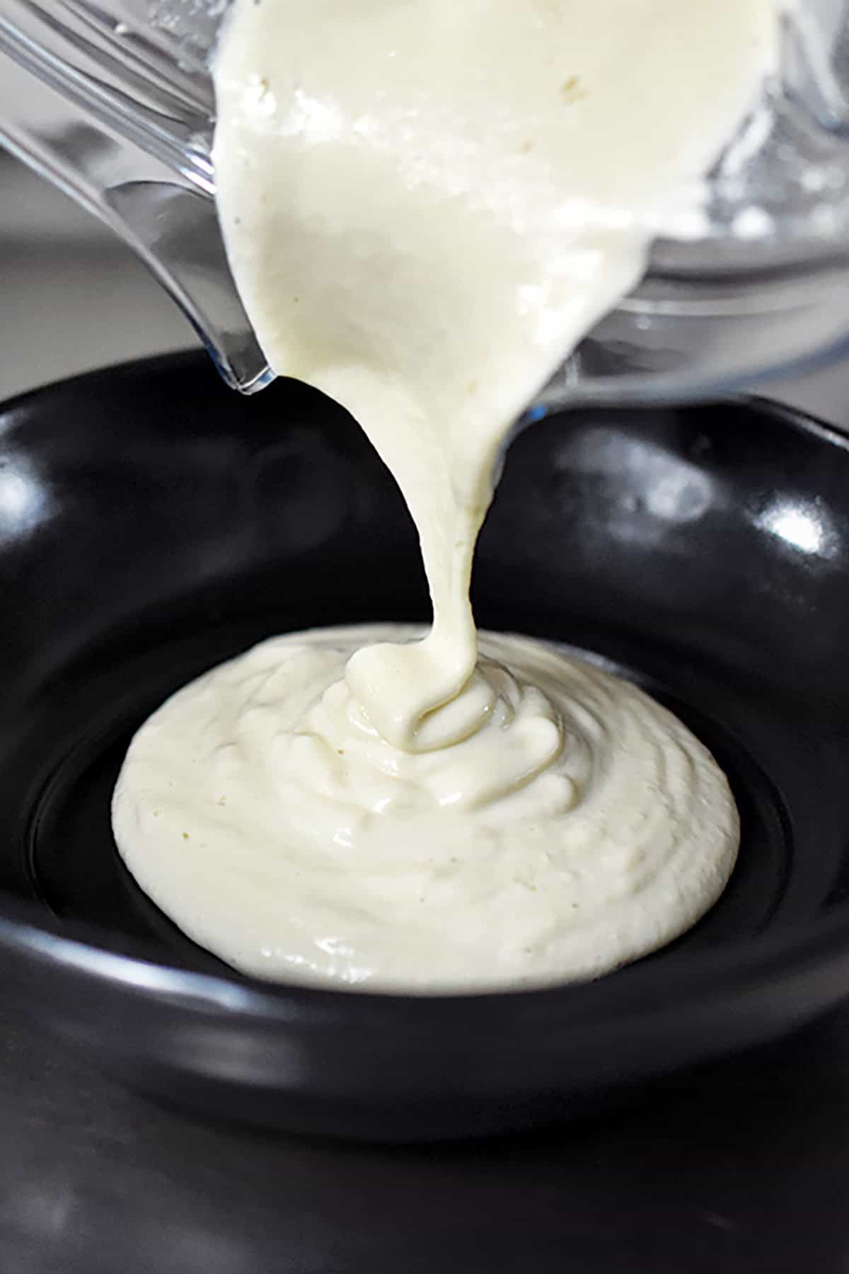 Pouring a creamy dairy-free cashew cream from a Vitamix blender into a serving bowl.