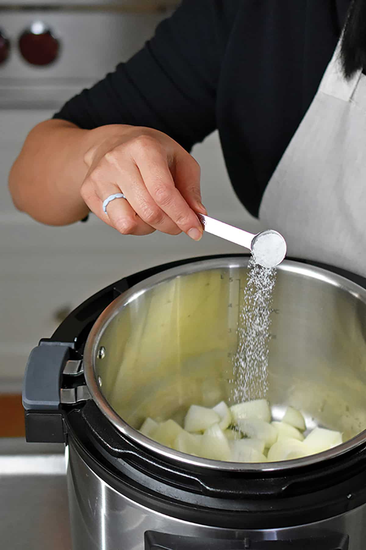 Adding a spoonful of salt to an open Instant Pot filled with chopped onions.