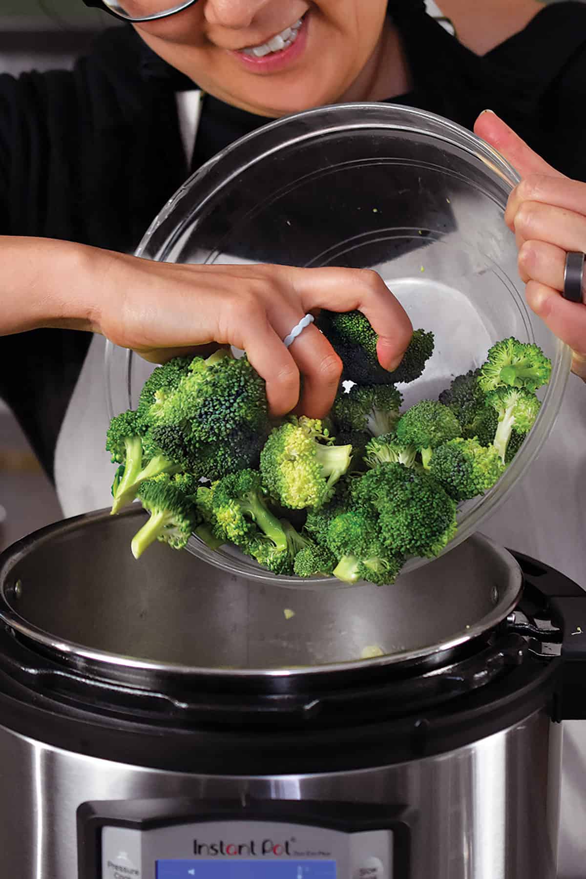 Adding chopped broccoli florets into an open Instant Pot to make green soup.