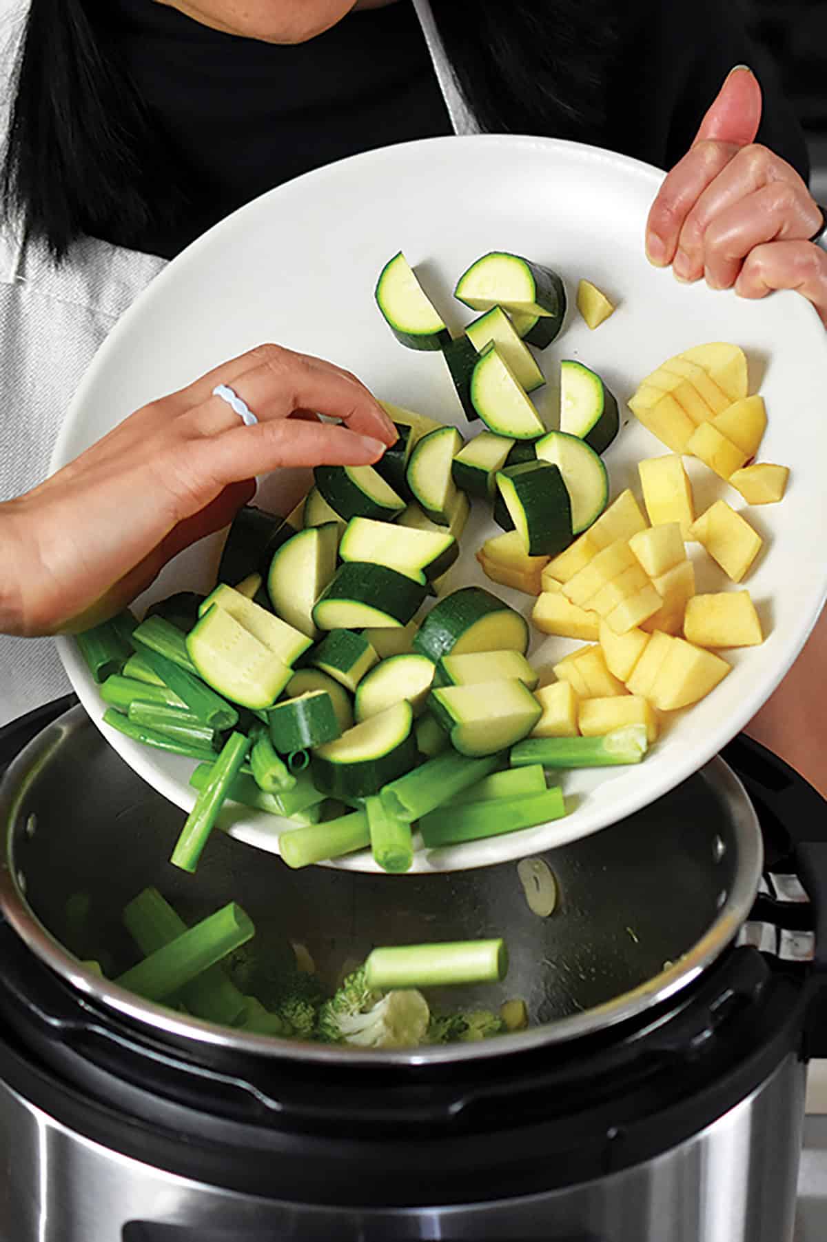 Adding chopped zucchini, green onions, and chopped apples to an open Instant Pot to make green soup.